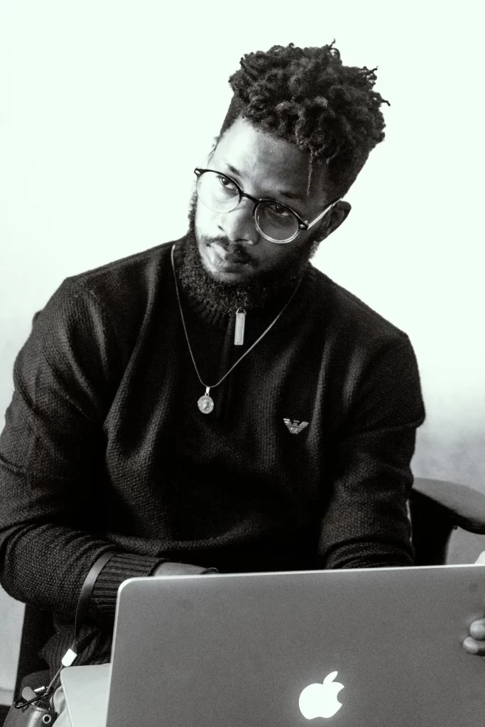 Black and white portrait of a black bearded man sitting in front of a macbook